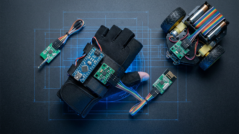 A glove with an MPU6050 gyroscope and Arduino Nano mounted on it, an nRF24L01 radio module, and a small two-wheeled robot on a dark workbench